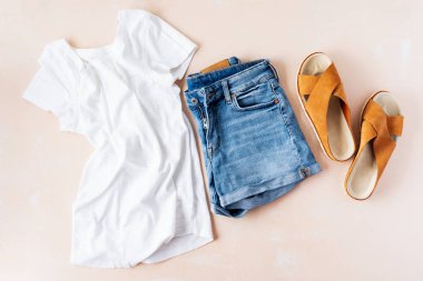 Pembe pastel arka plan üzerinde temel beyaz t-shirt, kot şort ve trendy deri sandalet