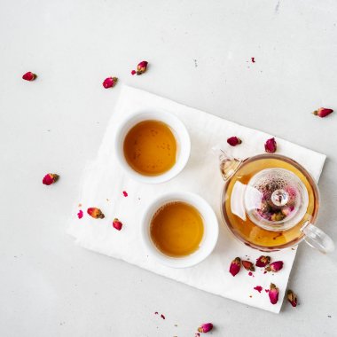 iki beyaz bardak ve gri taş arka planda kurutulmuş pembe gül tomurcukları bitkisel çay ile şeffaf çaydanlık