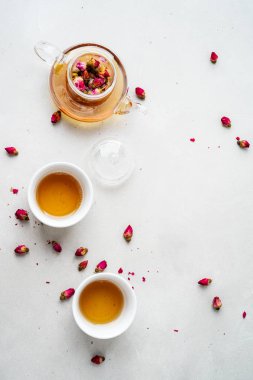 iki beyaz bardak ve gri taş arka planda kurutulmuş pembe gül tomurcukları bitkisel çay ile şeffaf çaydanlık