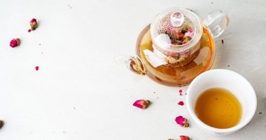 Beyaz seramik fincan ve gri arka planda kurutulmuş pembe güller bitkisel çay ile şeffaf çaydanlık