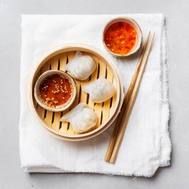Geleneksel Çince köfte Dim toplamları Har Gow sos ve yemek çubukları ile bambu gemi içinde ışık arka plan üzerinde buğulama