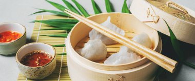 Geleneksel Çince köfte Dim toplamları Har Gow sos ve yemek çubukları ile bambu gemi içinde ışık arka plan üzerinde buğulama