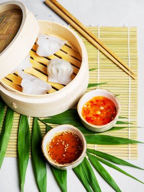 Geleneksel Çince köfte Dim toplamları Har Gow sos ve yemek çubukları ile bambu gemi içinde ışık arka plan üzerinde buğulama