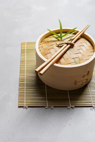 Traditional chinese bamboo steamer for steamed dumplings Dim Sums with chopsticks on light surface with copy space. Asian food background.