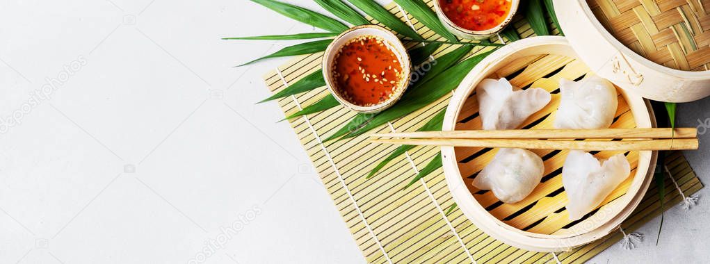 Traditional chinese steamed dumplings Dim Sums HAR GOW in bamboo steamer with sauce and chopsticks on light background