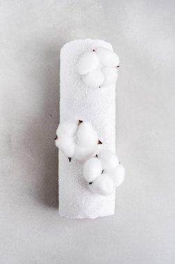 Beyaz kabarık havlu gri taş arka planda doğal pamuk çiçekleri ile rulo içine bükülmüş