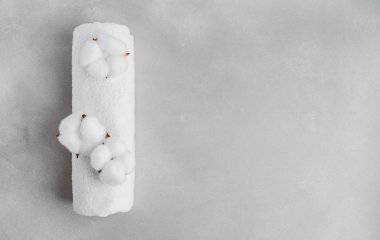 Beyaz kabarık havlu gri taş arka planda doğal pamuk çiçekleri ile rulo içine bükülmüş