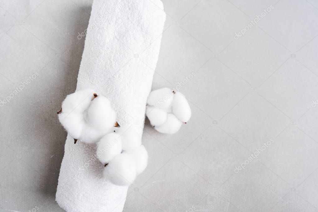 White fluffy towel twisted into roll with flowers of natural cotton on gray stone background