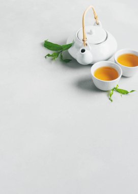 Çay ve çaydanlık beyaz bardak gri arka plan üzerinde yeşil yaprakları ile çevrili