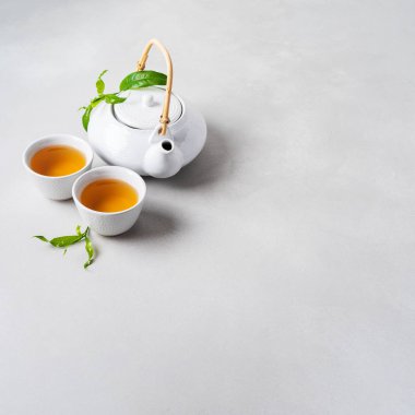 Çay ve çaydanlık beyaz bardak gri arka plan üzerinde yeşil yaprakları ile çevrili