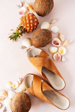 Pembe pastel arka plan üzerinde deri trendy parmak arası terlik, kabuklar ve tropikal meyvelerüst görünümü