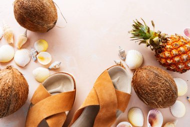 Pembe pastel arka plan üzerinde deri trendy parmak arası terlik, kabuklar ve tropikal meyvelerüst görünümü