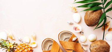 Pembe pastel arka plan üzerinde deri trendy parmak arası terlik, kabuklar ve tropikal meyvelerüst görünümü