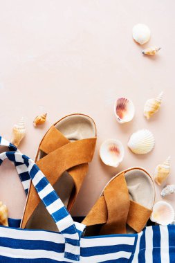 Pembe pastel arka planda rahat trendy deri sandalet ve kabukları ile çizgili plaj çantası