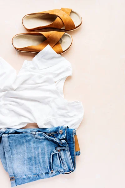 Basic white t-shirt, denim shorts and trendy leather sandals on pink pastel background