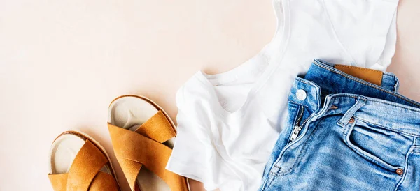 Basic white t-shirt, denim shorts and trendy leather sandals on pink pastel background