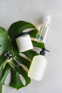 Yeşil monstera yaprağı ile gri arka plan üzerinde kozmetik ambalaj için şişe kozmetik seti
