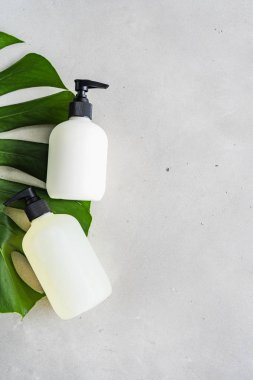 Yeşil monstera yaprağı ile gri arka plan üzerinde kozmetik ambalaj için şişe kozmetik seti