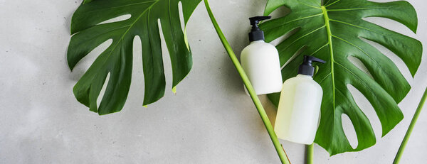 Косметический набор бутылок для упаковки на сером бетонном фоне с зелеными листьями
