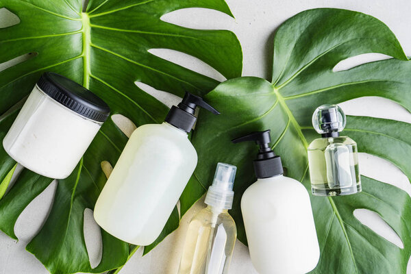 Cosmetic set of bottles for packaging on grey concrete background with green leaves