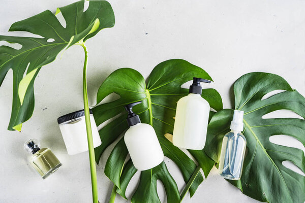 Cosmetic set of bottles for packaging on grey concrete background with green leaves