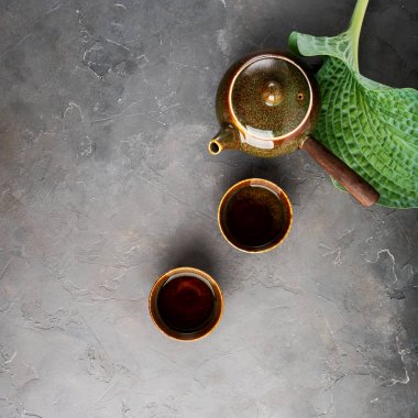 Gri beton arka plan üzerinde çay fincanları ve yeşil yaprak ile yan kolu ile Geleneksel kil Japon çaydanlık kyusu