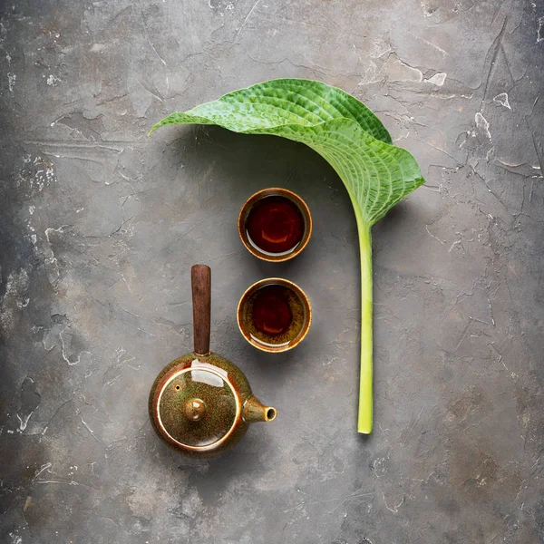 Gri beton arka plan üzerinde çay fincanları ve yeşil yaprak ile yan kolu ile Geleneksel kil Japon çaydanlık kyusu