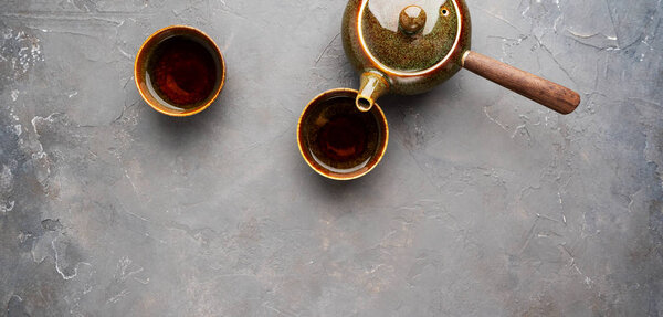 Top view of traditional clay japanese teapot kyusu with side handle with two teacups on gray concrete background