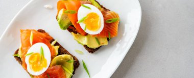 Beton arka plan üzerinde avokado, somon, yumurta ve doğranmış bahar soğan ile kepekli tost sandviç 