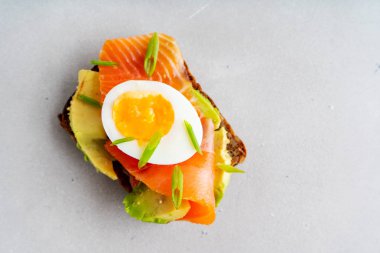 Beton arka plan üzerinde avokado, somon, yumurta ve bahar soğan ile çok tahıllı kepekli tost sağlıklı sandviç