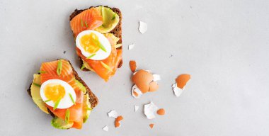 Avokado, somon, yumurta ve kırık yumurta kabuğu ile beton arka plan üzerinde doğranmış bahar soğan ile kepekli tost sandviç 