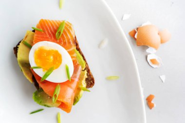 Beyaz tabak arka planda avokado, somon, yumurta ve bahar soğan ile çavdar tost üzerinde sandviç üst görünümü