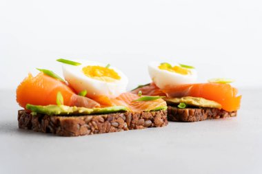 Beton arka plan üzerinde avokado, somon, yumurta ve doğranmış bahar soğan ile kepekli tost sandviç 