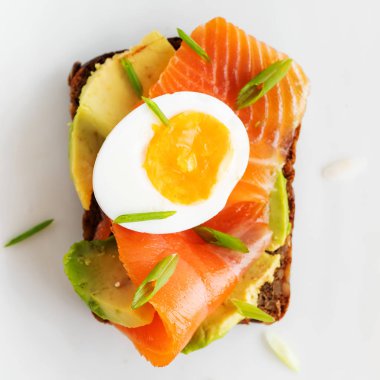 Beyaz tabak arka planda avokado, somon, yumurta ve bahar soğan ile çavdar tost üzerinde sandviç üst görünümü