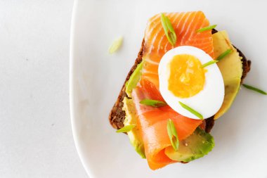 Beyaz tabak arka planda avokado, somon, yumurta ve bahar soğan ile çavdar tost üzerinde sandviç üst görünümü