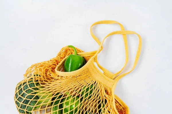 Top view of fresh green vegetables in net bag on white concrete background