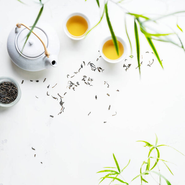 Asian set with green tea, cups and teapot on white background with green leaves 