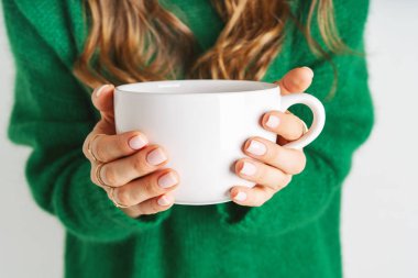 Elinde büyük beyaz kupa tutan sıcak yün yeşil kazak kadın