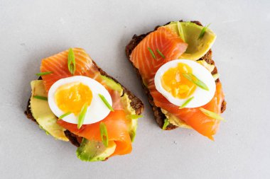 Beton arka plan üzerinde avokado, somon, yumurta ve doğranmış bahar soğan ile kepekli tost sandviç yakın görünümü 