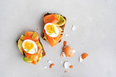 Beton arka plan üzerinde avokado, somon, yumurta ve doğranmış bahar soğan ile kepekli tost sandviç yakın görünümü 