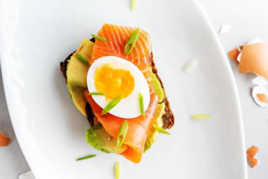 Beyaz tabak arka planda avokado, somon, yumurta ve bahar soğan ile çavdar tost üzerinde sandviç üst görünümü