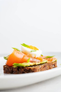 Top view of sandwich on rye toast with avocado, salmon, egg and spring onion on white plate background clipart