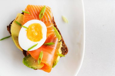 Beyaz tabak arka planda avokado, somon, yumurta ve bahar soğan ile çavdar tost üzerinde sandviç üst görünümü