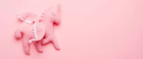 Felt toy unicorn from baby mobile on pink background.