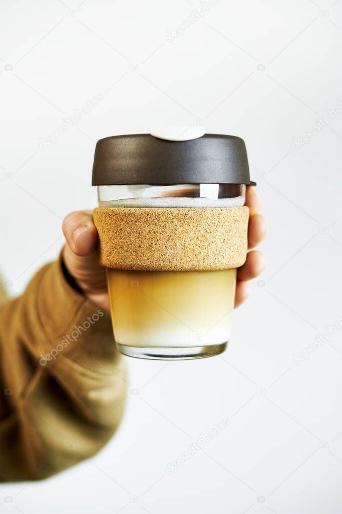 Female hands hold a reusable travel glass mug for take away coffee on white background. Eco-friendly concept. Zero waste. Sustainable lifestyle concept.