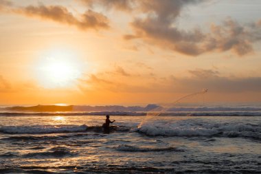 Bir balıkçı şafakta denize bir ağ atar. Bali 'nin doğu kıyısındaki Pantai Pabean Ketewel Sahili' nde güzel bir gün doğumu..