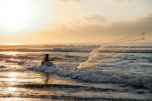 Bir balıkçı şafakta denize bir ağ atar. Bali 'nin doğu kıyısındaki Pantai Pabean Ketewel Sahili' nde güzel bir gün doğumu..
