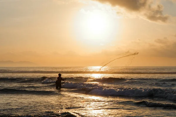 Bir balıkçı şafakta denize bir ağ atar. Bali 'nin doğu kıyısındaki Pantai Pabean Ketewel Sahili' nde güzel bir gün doğumu..
