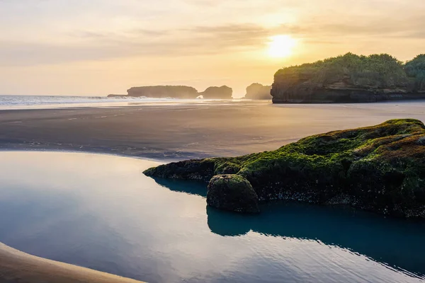 Idyllic manzara. Sahilde gün batımı kayalarla. Gökyüzünün yansıdığı bir su birikintisi. Tonal perspektif. Arka plandaki sisli kayalıklar.
