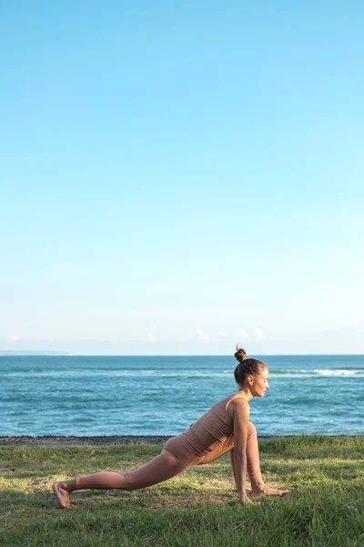 Eşofmanlı güzel genç bir kadın yoga hareketlerine hazırlanıyor. Kız okyanus kıyısındaki çimlere spor yapmaya gider. Tam boy dişi bir yogi yan yana durur..